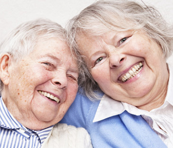 Two senior adult females smiling with one putting her arm across the other woman's shoulder